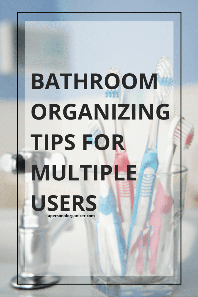 A clear cup holds several colorful toothbrushes on a bathroom sink, with text overlay: “Bathroom Organizing Tips for Multiple Users.” The softly blurred background highlights simple bathroom organizing solutions.