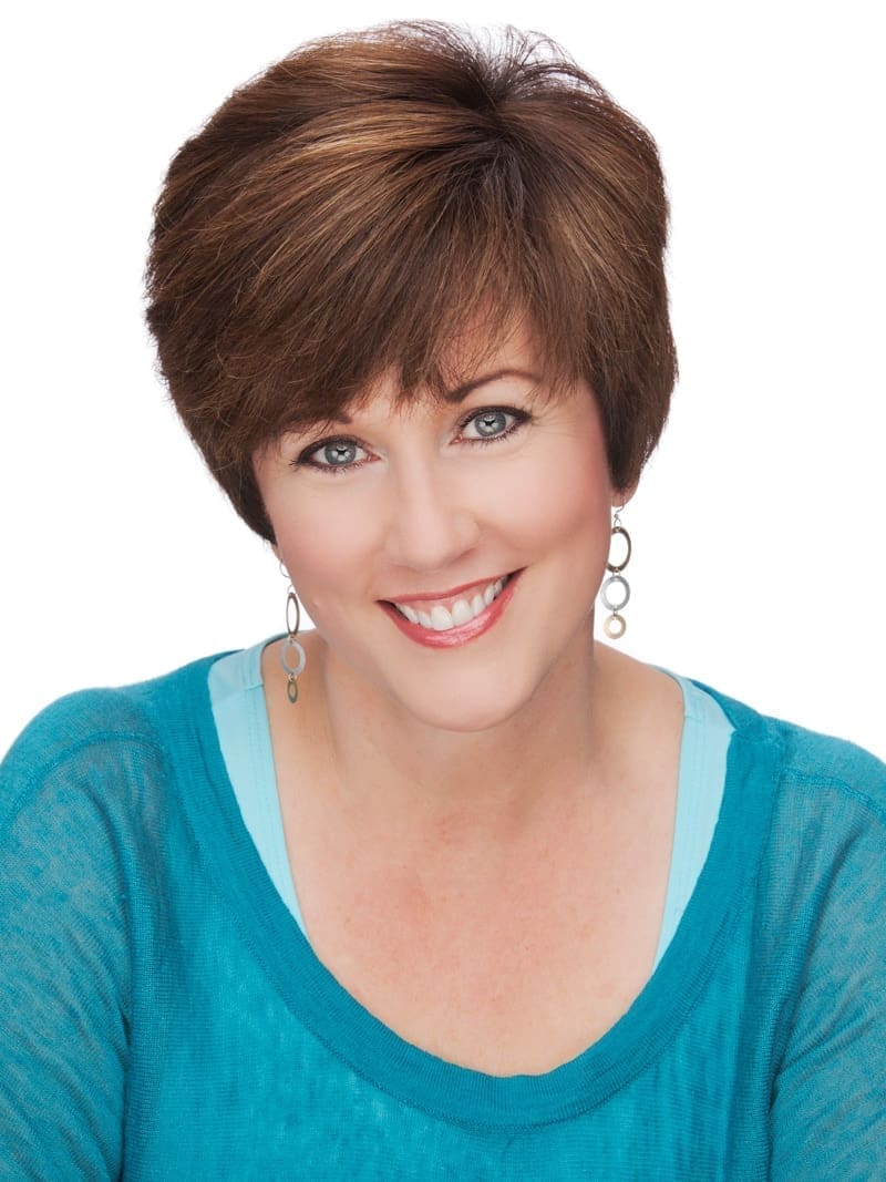A woman with short brown hair smiles at the camera. She is wearing a turquoise top over a light blue undershirt and round earrings. The background is plain white, giving her the air of someone ready to teach you how to become a professional organizer.