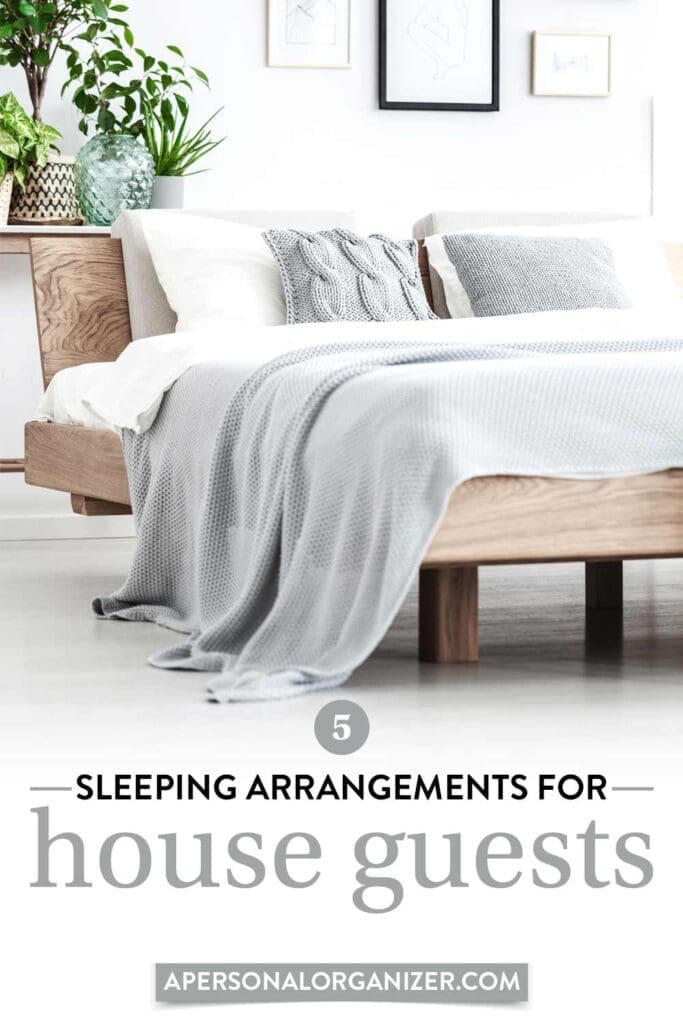 A modern bedroom designed for small living, featuring a wooden bed frame, white sheets, and a light gray knit blanket. Decorative pillows are neatly arranged at the head. Above the bed hang framed pictures, with a potted plant on the bedside table. Text reads "Sleeping Arrangements for House Guests.