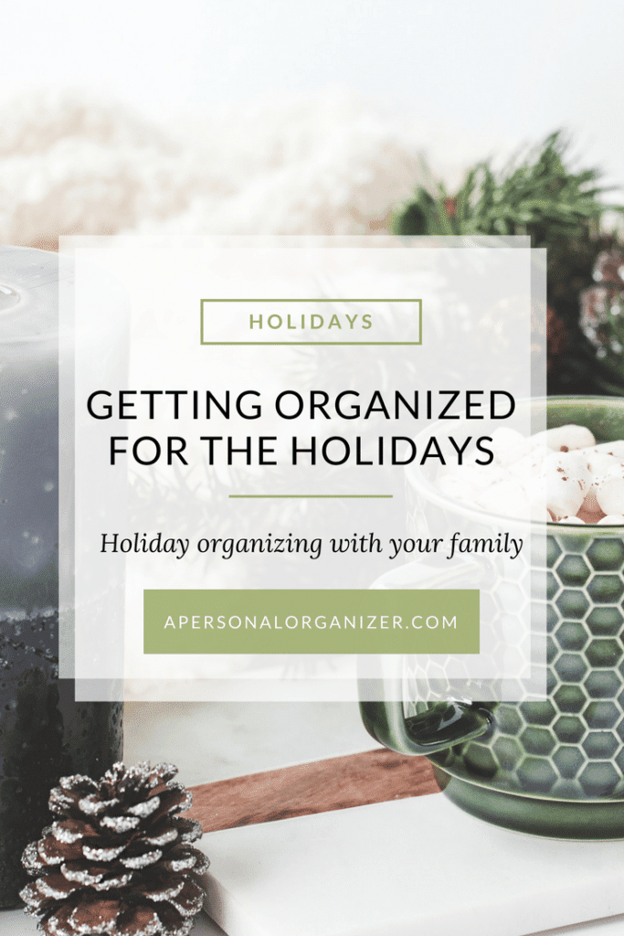 A serene holiday-themed setup featuring a green mug topped with marshmallows, a pine cone, and some greenery. Overlaid text reads, “Holiday Organizing for the Season - Holiday organizing with your family” along with “apersonalorganizer.com” at the bottom.