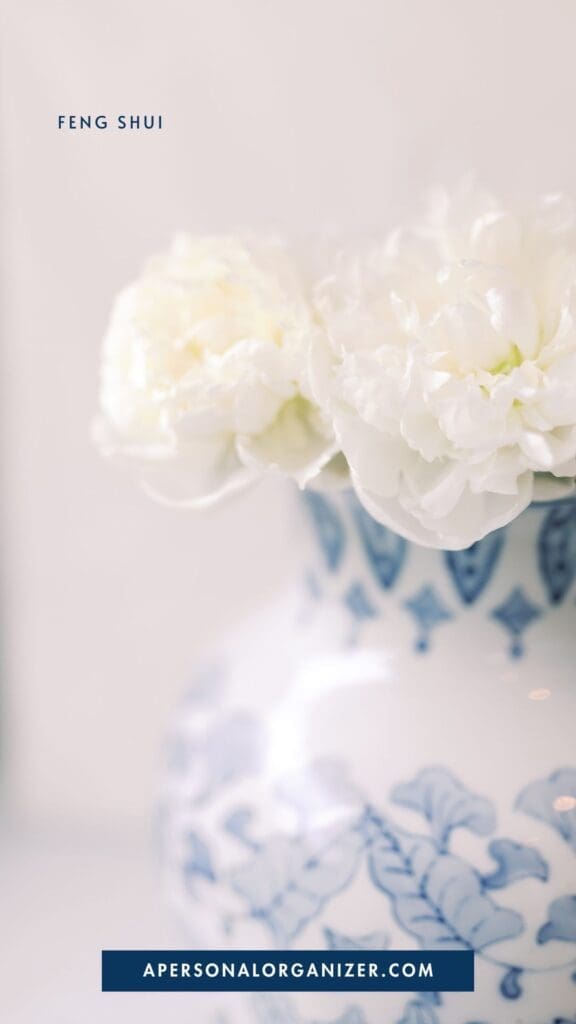 A close-up of white flowers in a blue and white porcelain vase with "FENG SHUI" above, "APERSONALORGANIZER.COM" below, and a soft light background—perfect inspiration for declutter and organizing enthusiasts.