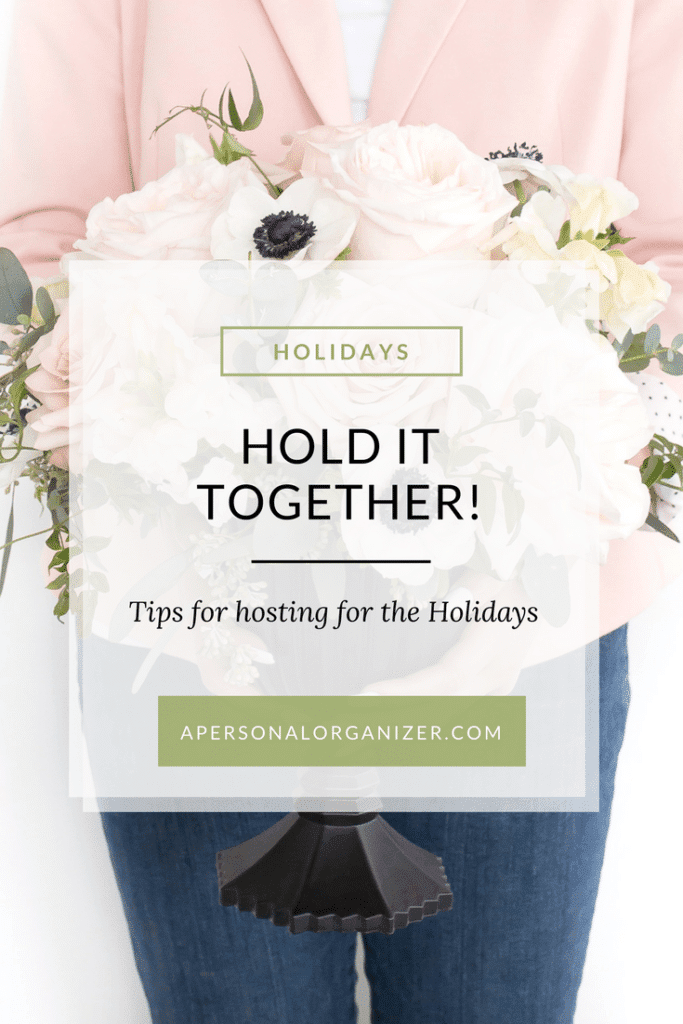 A person wearing a pink blazer and blue jeans holds a bouquet of white and light pink flowers. The bouquet features a sign that reads "HOLIDAYS, HOLD IT TOGETHER! Tips for hosting for the Holidays." Below the message is the website address apersonalorganizer.com.