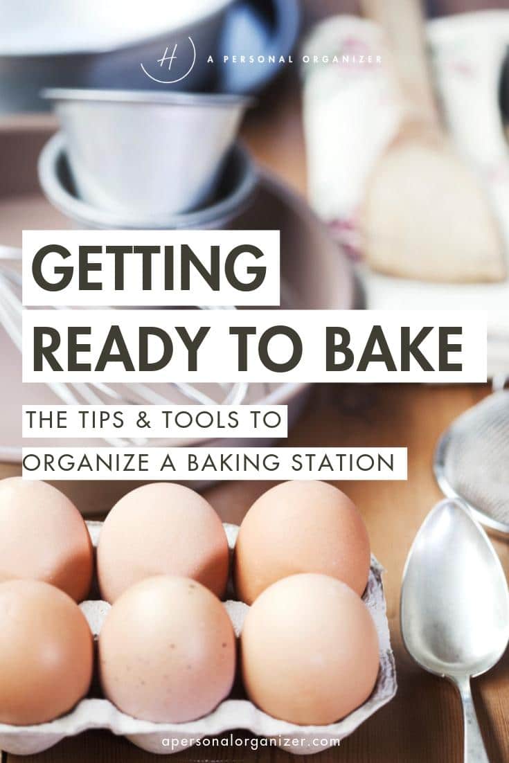 A close-up of a baking station with eggs in a cardboard carton and a handy baking ingredients organizer. In the background, various tools and ingredients are partially visible. Text overlay reads: "Getting Ready to Bake: The Tips & Tools to Organize a Baking Station.