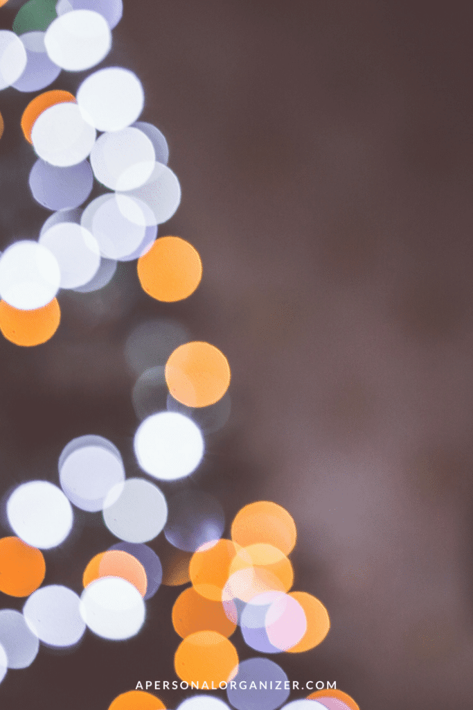 A blurred image of glowing lights in circular shapes of various sizes, predominantly in white and orange hues, set against a muted background. The text "APERSONALORGANIZER.COM" is displayed at the bottom center of the image, offering a subtle reminder to feng shui your holidays.