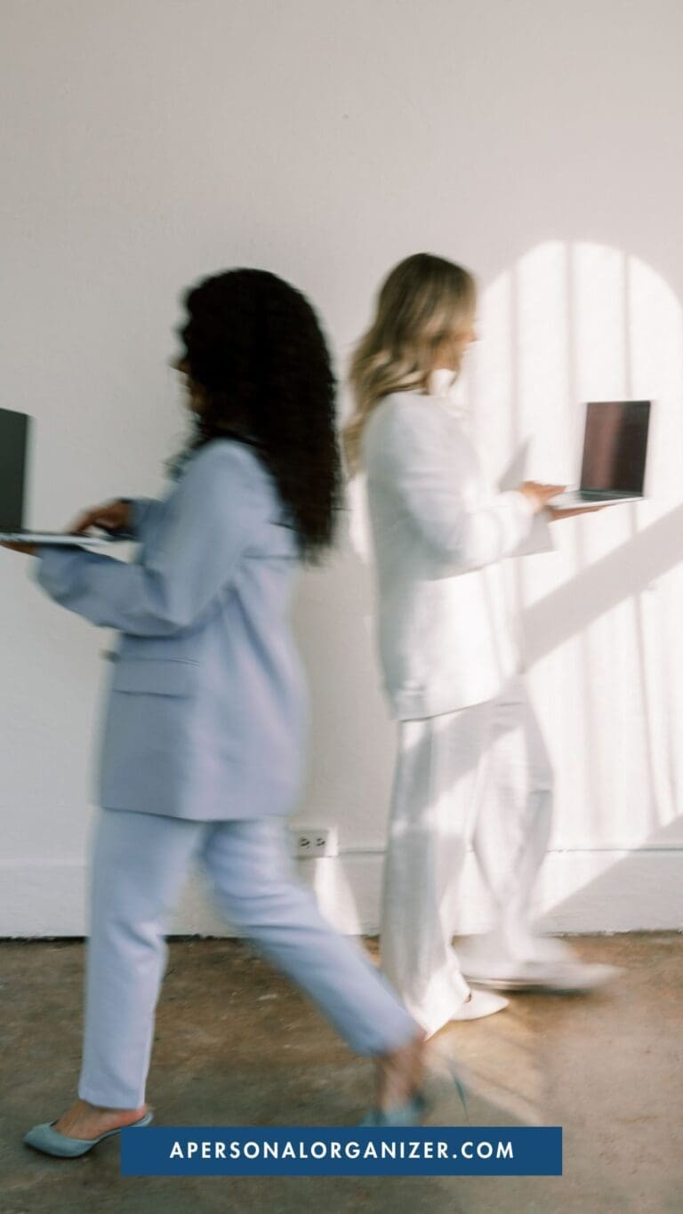 Two women in business attire walk past each other with open laptops, blurred in motion against a white wall. Sunlight casts shadows as they stride purposefully—declutter your workflow today. A website link appears at the bottom.