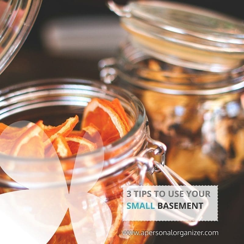 Close-up photo of two glass jars with metal clasps filled with dried fruit. A white transparent bow overlays the lower-left corner. The text reads, "3 Tips to Organize Your Small Basement" with a website link "apersonalorganizer.com" in the lower-right corner.