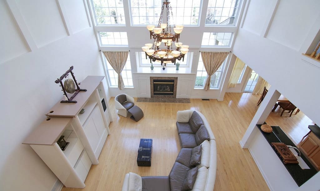 A bright, spacious living room with light wood floors, a gray sectional sofa, a fireplace, large windows with curtains, a chandelier, and modern furniture—perfect for your next home tour—viewed from above.