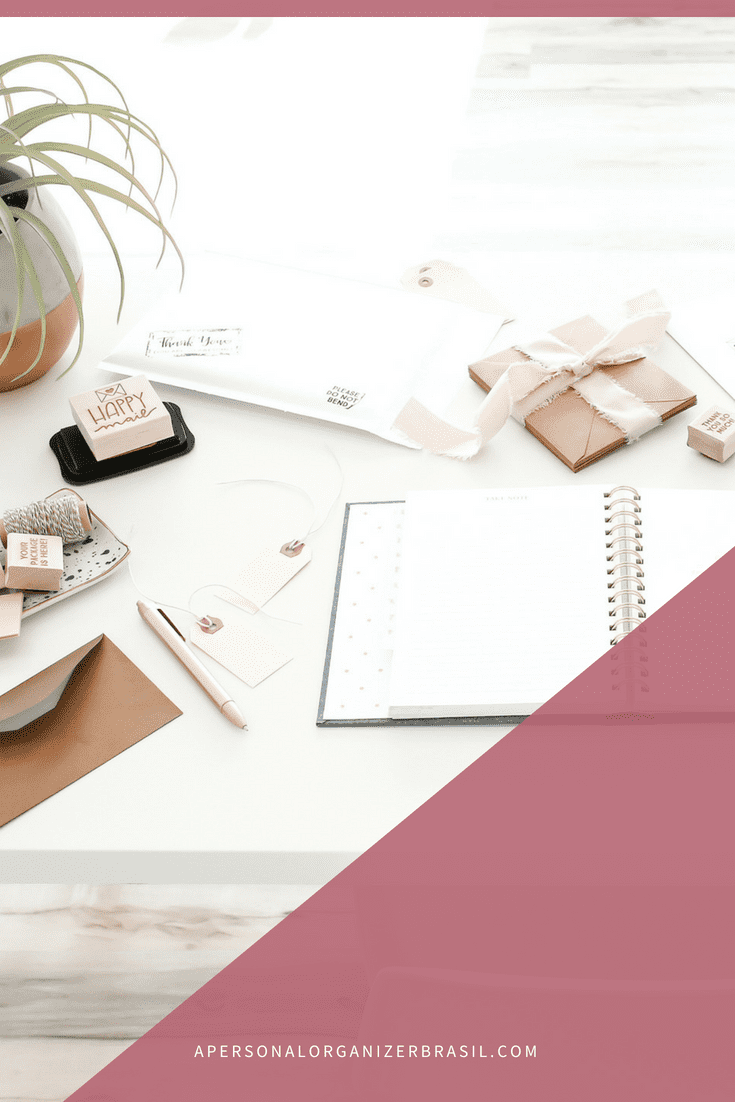 A tidy desk with a plant, wrapped gifts, stationery, open notebook for blocos de tempo planning, envelopes, tags, a stamp, and a pink pen. A pink overlay covers the bottom right corner with a website: apersonalorganizerbrasil.com.
