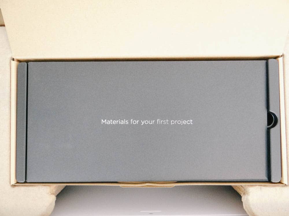 A cardboard box opened to reveal a smaller, sleek black box inside. The black box, designed for Cricut Maker enthusiasts, has the text "Materials for your first project" written in white letters on its center.