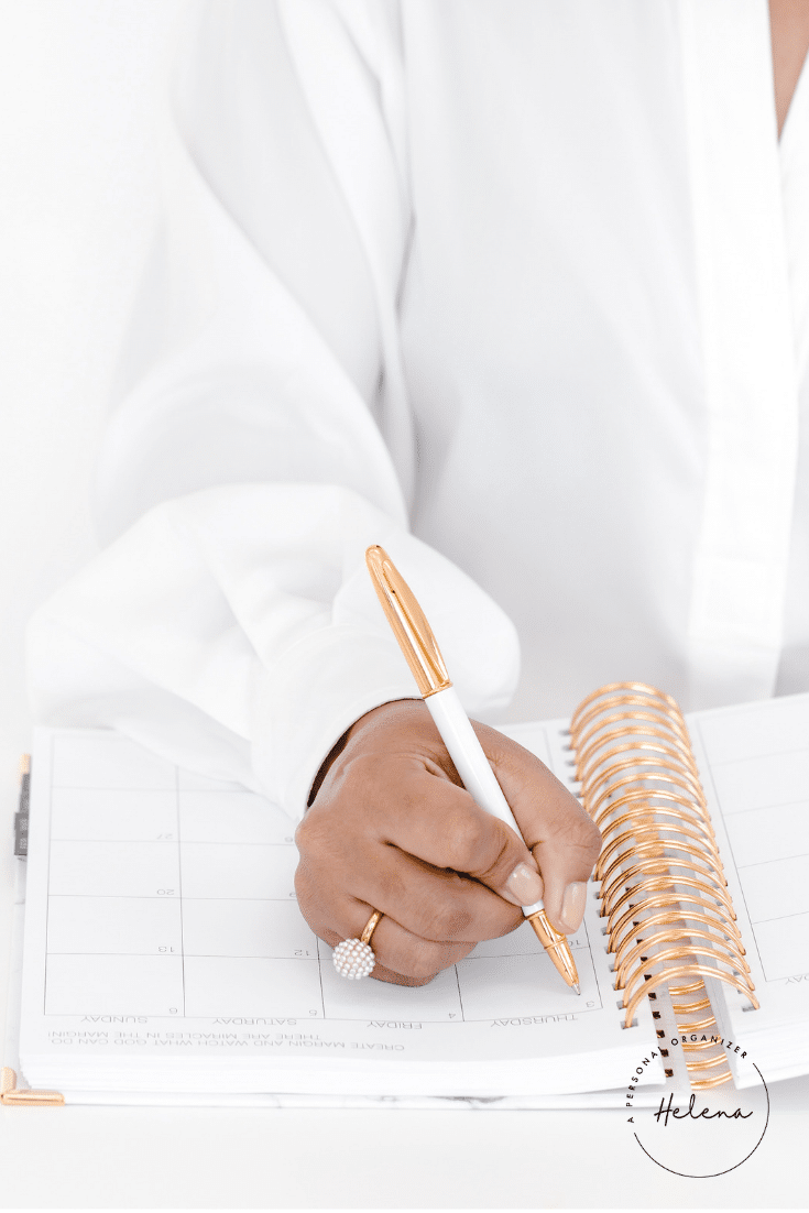 A person wearing a white shirt and pearl ring writes email subscriber ideas in a spiral-bound planner with a gold and white pen. The clean, minimal scene focuses on the hand and planner, perfect for organizing free content strategies.