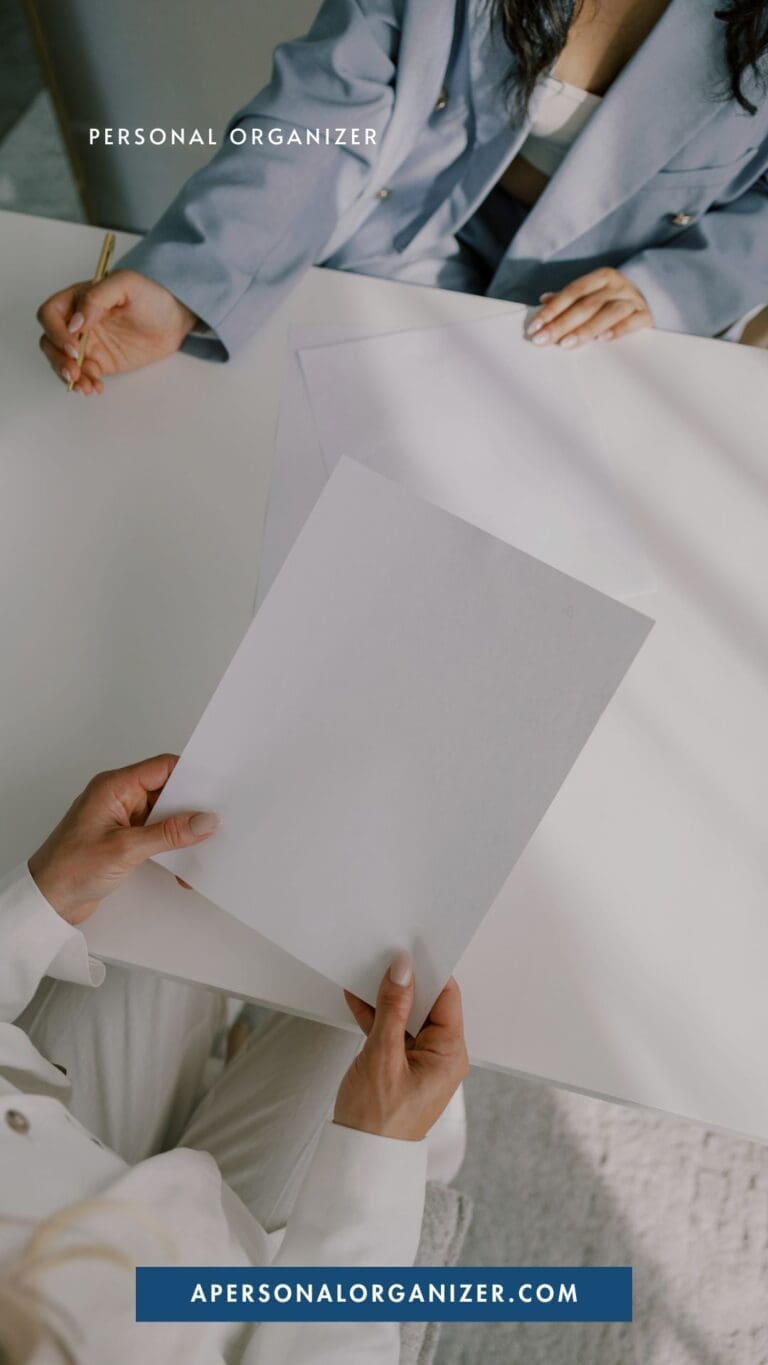 Two people sitting at a table, one holding a blank sheet of paper, the other writing—ready to tackle clutter and embrace better organization. Text on the image reads “PERSONAL ORGANIZER” and “APERSONALORGANIZER.COM.”.