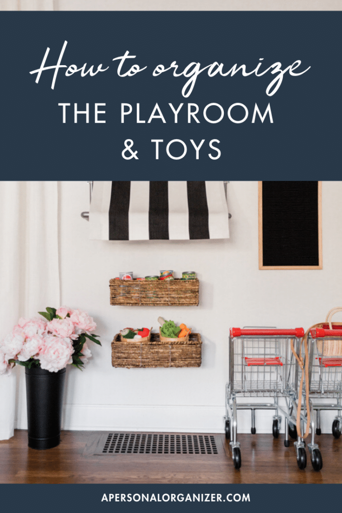 Playroom organization made easy: Two baskets hold toys while two small shopping carts add charm. A handy blackboard hangs above, and a black vase with pink flowers sits elegantly on the floor. Discover tips on organizing playrooms and toys efficiently.