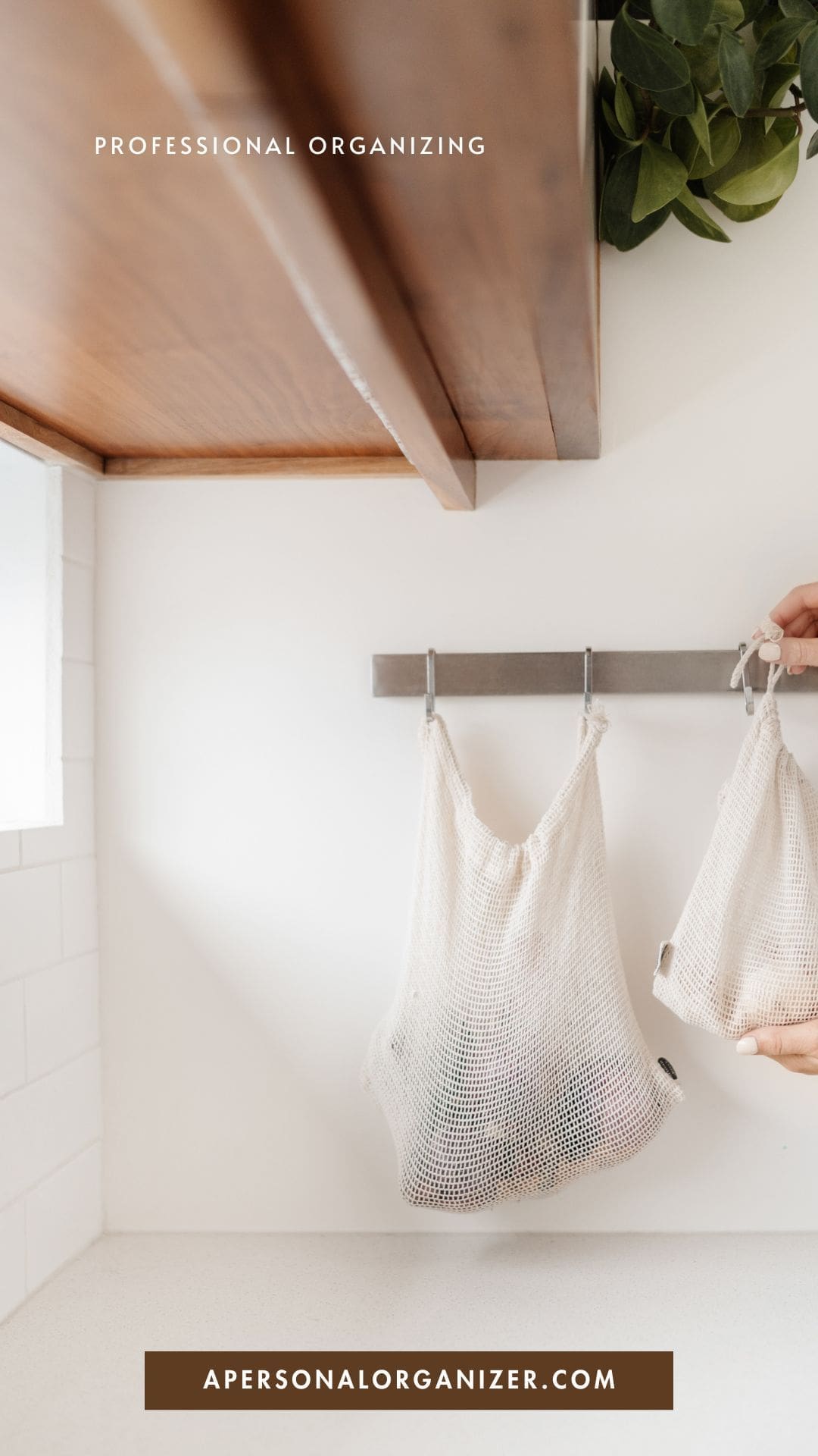 A hand hangs a reusable mesh bag on a hook under a wooden shelf in a bright, minimalist kitchen—perfect for declutter and professional organizing. Text reads "Professional Organizing" at the top and "apersonalorganizer.com" at the bottom.