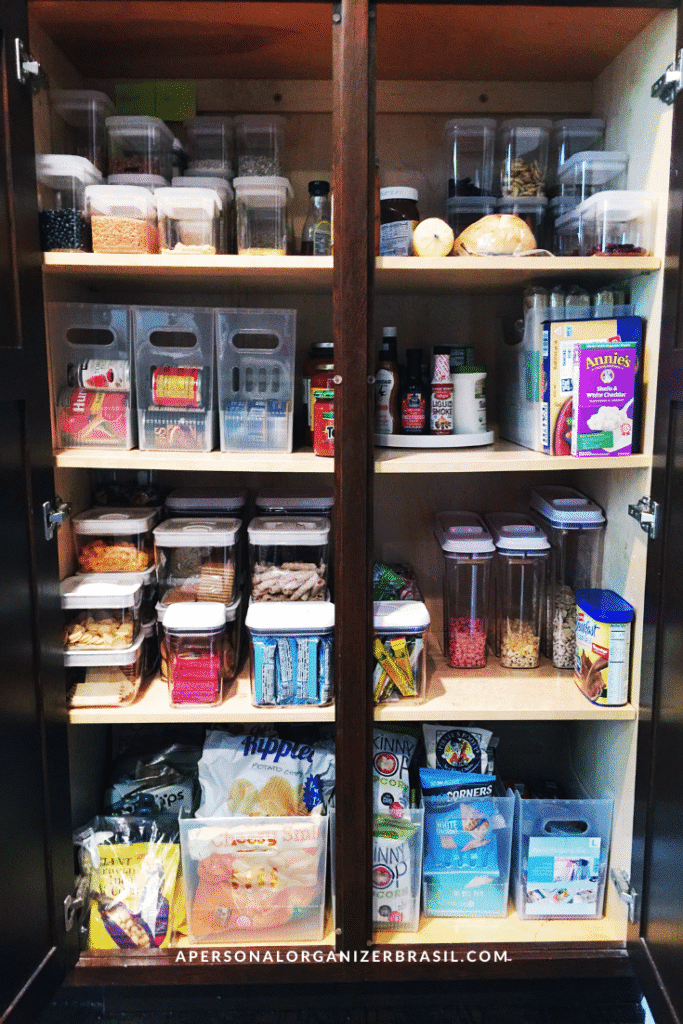 A neatly organized pantry highlights how to organizar a despensa, with shelves holding clear containers of cereals, grains, snacks, and canned goods—all arranged for easy access and perfect visibility.
