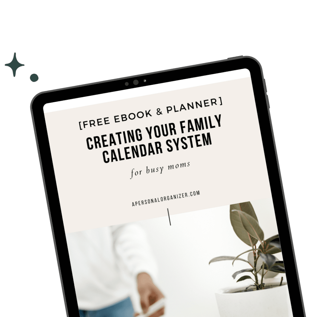A tablet showcases the ebook "Creating Your Family Calendar System for Busy Moms." This free resource is perfect for those looking to organize their hectic schedules. A person in a light shirt appears behind the tablet, with a lush green plant adding life to the scene on the right.
