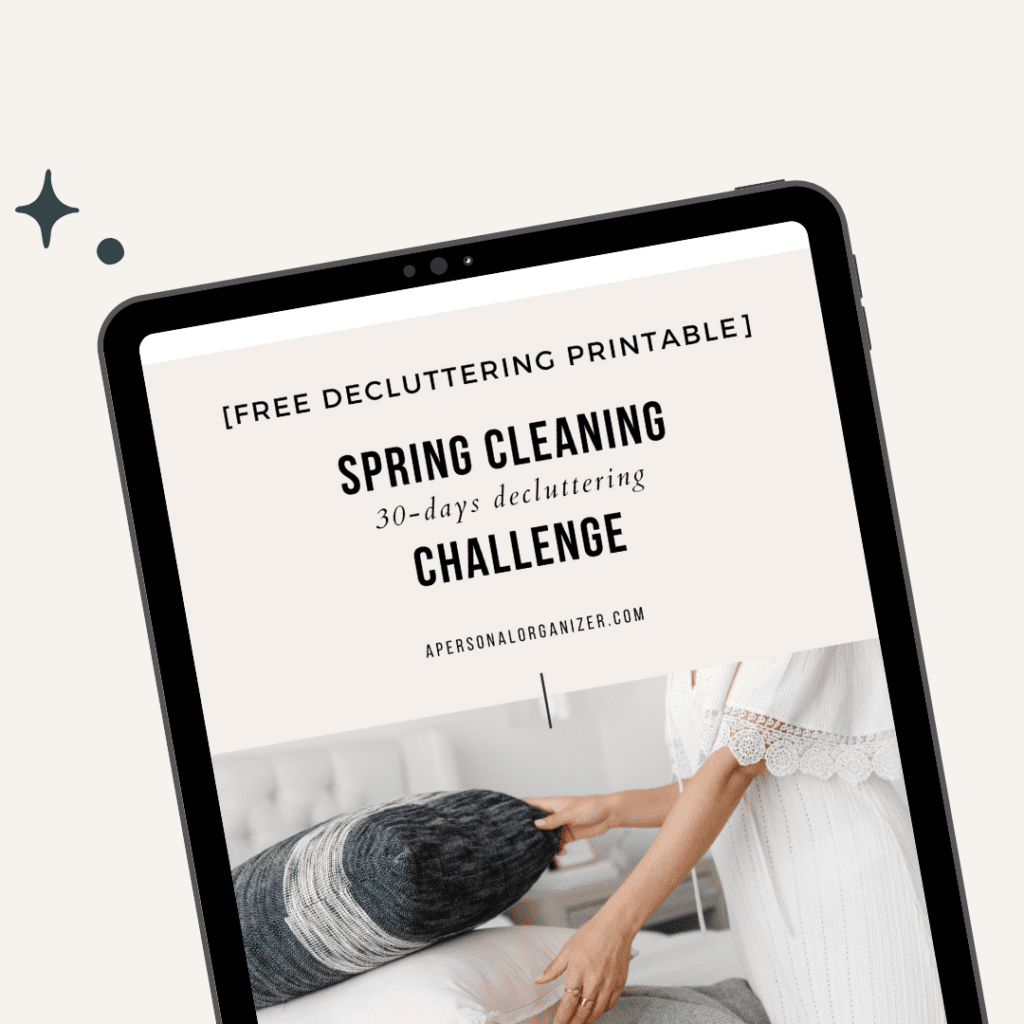 A tablet displays a digital document titled "Spring Cleaning 30-days Decluttering Challenge" with a subtitle "[Free Decluttering Printable]" from apersonalorganizer.com. The background features a person in a white dress organizing pillows, adding a touch of harmony to the serene setting.