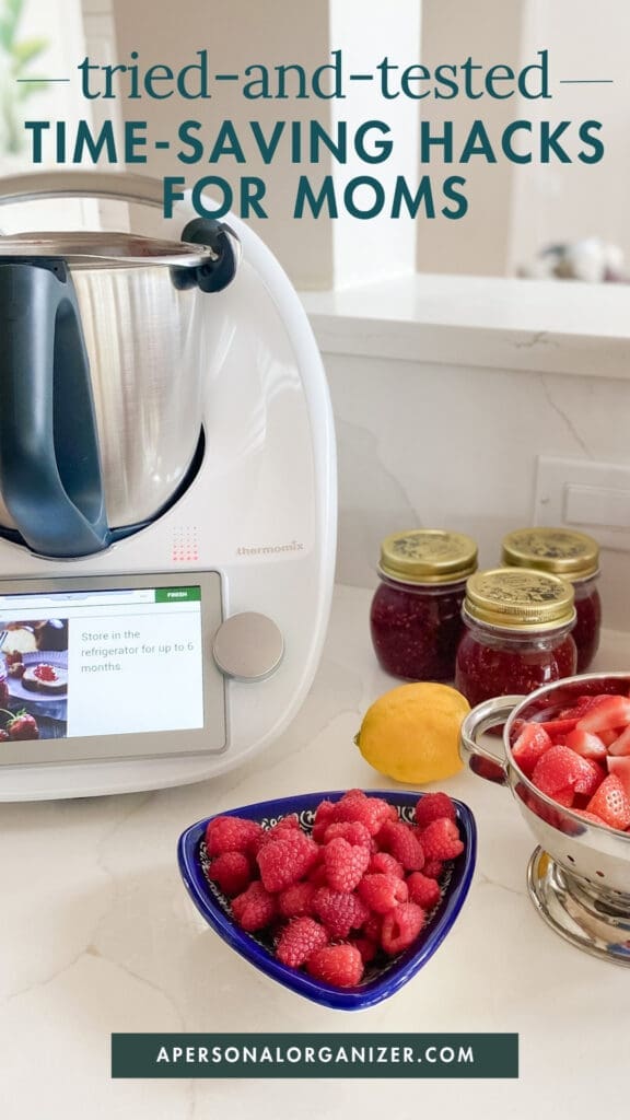 A kitchen counter with a Thermomix appliance, jars of homemade jam, a lemon, a bowl of strawberries, and raspberries. Text reads: "Discover tried-and-tested time saving hacks for moms.