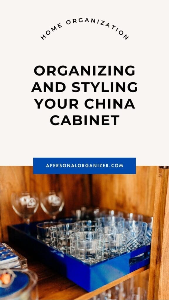 A wooden china cabinet with neatly arranged glassware and a blue tray, featuring text about organizing and styling a china cabinet for home organization.