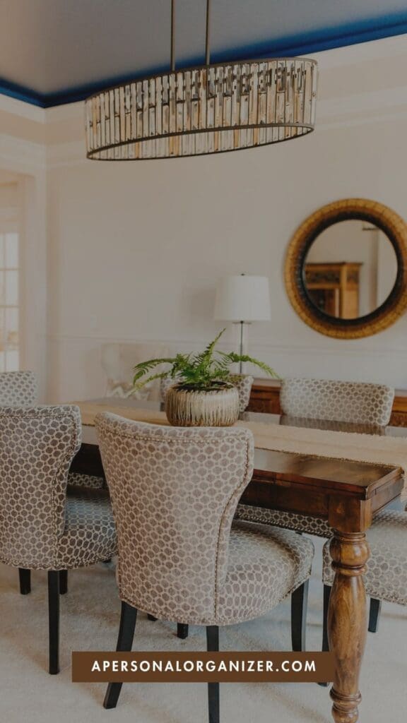 A decluttered dining room featuring a wooden table, patterned chairs, a fern centerpiece, and a circular wall mirror under an oval crystal chandelier.
