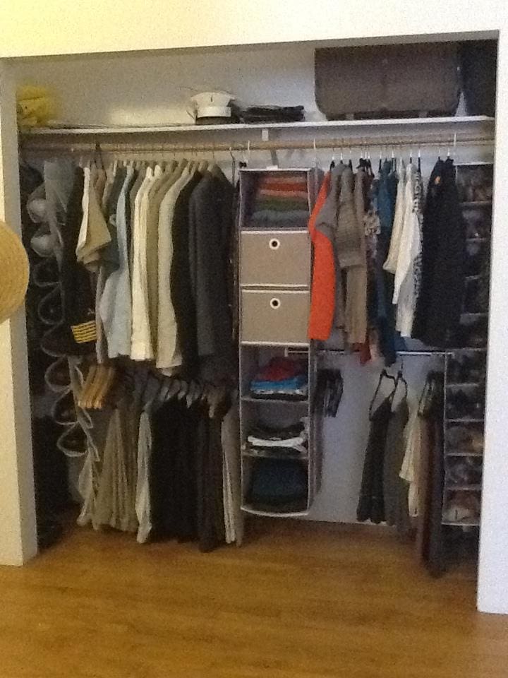 The closet is well-organized with two sections of clothing hanging on hangers. On the left, jackets and shirts are neatly arranged, with hats stored above. In the middle, a fabric organizer efficiently holds folded clothes. More shirts and pants hang on the right, while shoes are neatly aligned at the bottom.