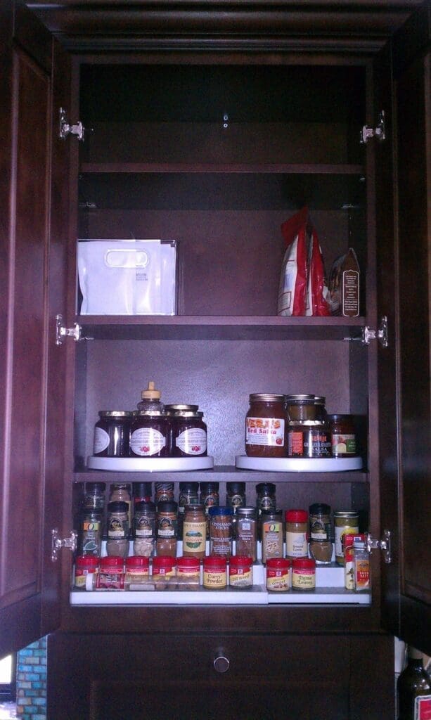 The open drawer, expertly organized, is filled with various kitchen appliances and tools, including a colander, blender base, and other accessories. The wooden drawer with a metal handle sits neatly next to a stainless steel appliance.