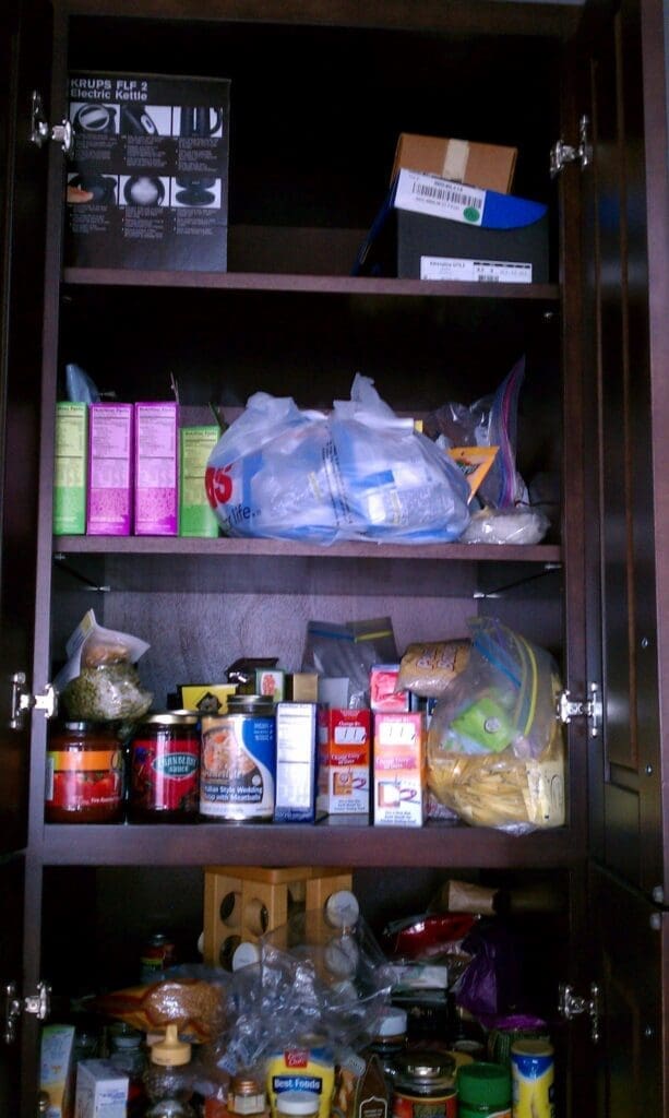 A meticulously organized pantry cupboard. Shelves brimming with jars, bottles, and boxes create a symphony of canned goods, pasta, and snacks. The top shelf neatly categorizes miscellaneous items in an array of plastic bags and boxes, reflecting an artful blend of efficiency and order.