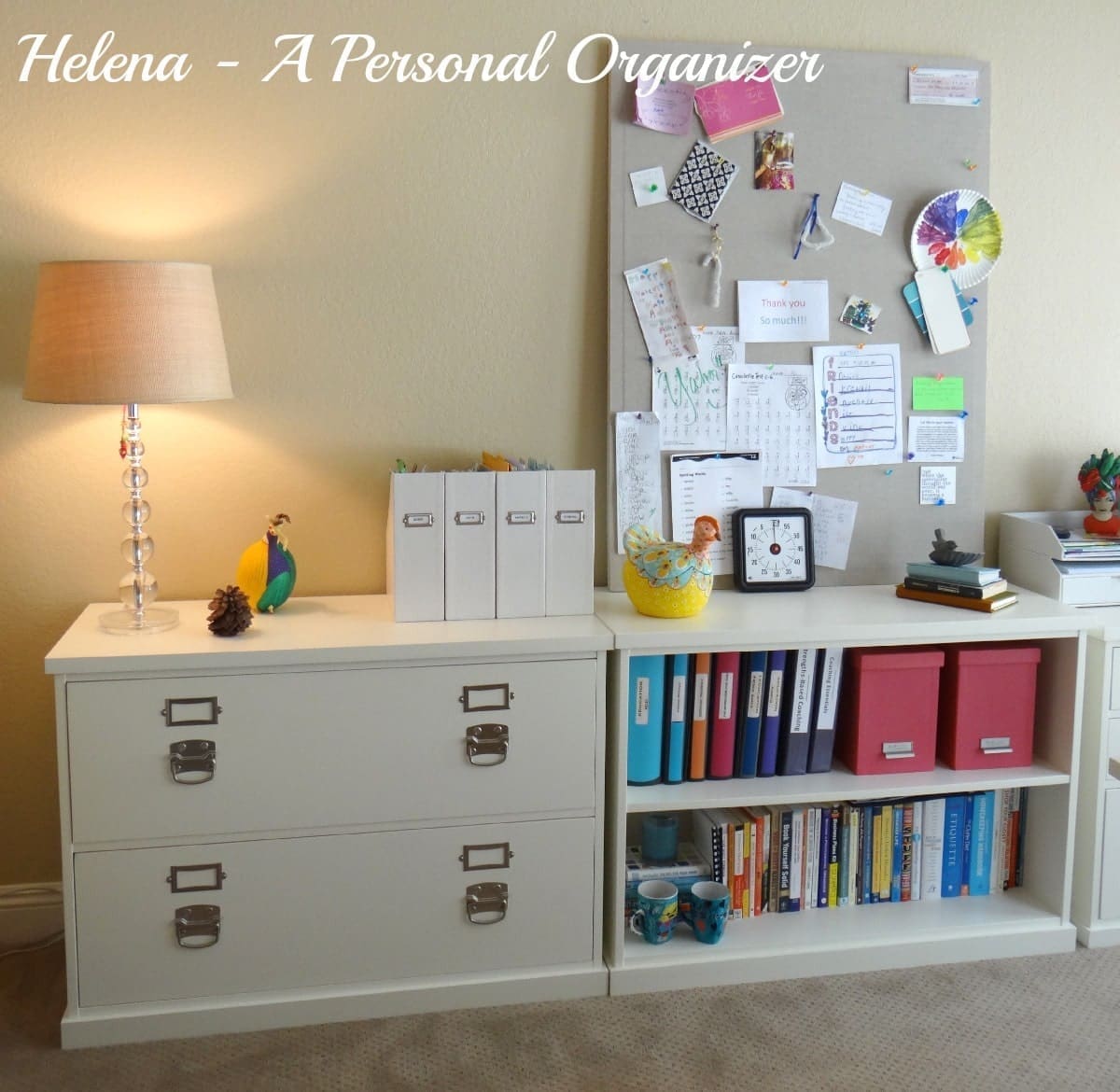 A neatly organized home office nook features a lamp on a filing cabinet, a decorative bird, file boxes, and a corkboard with various notes and decorations. Perfect for back-to-school season, it includes a white shelf with books, binders, and small storage containers to complete the setup.