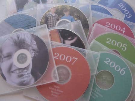 A collection of CDs in transparent plastic cases is displayed. Each CD, dated from 2003 to 2007, showcases photo organizing at its finest. Some CDs feature photos of people and a cat, while others are plain with just the year visible.