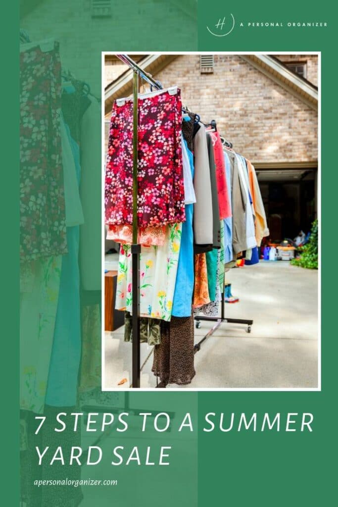 Clothing and fabric are displayed on racks outside a garage, inviting you to explore. The text reads "7 Steps to a Successful Summer Yard Sale" at the bottom, with "apersonalorganizer.com" beneath. A green overlay partially frames this vibrant yard sale scene.