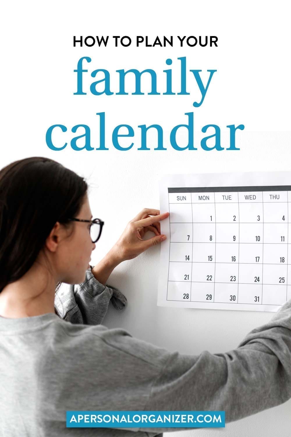 Person hanging a calendar on a white wall in a cozy corner. The text above reads, "How to plan your family calendar for small living." At the bottom, the text displays "apersonalorganizer.com.