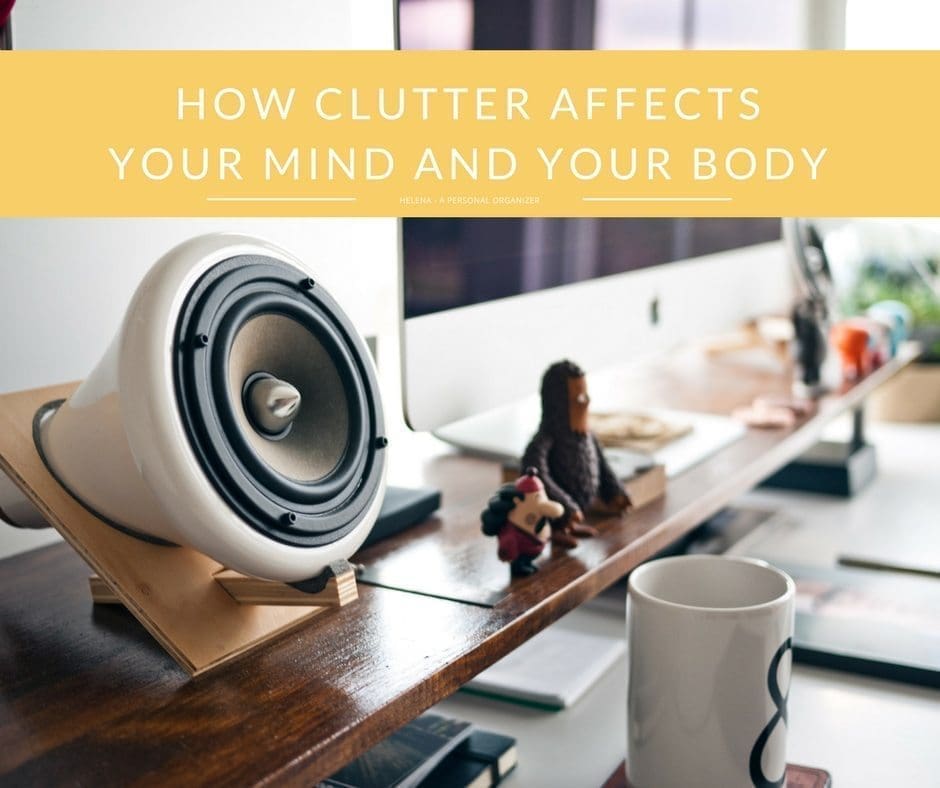 A tidy desk setup features a computer monitor, a stylish speaker, a few decorative items, and a mug. The text "How Clutter Affects Your Mind And Your Body" is prominently displayed on a yellow banner at the top of the image.