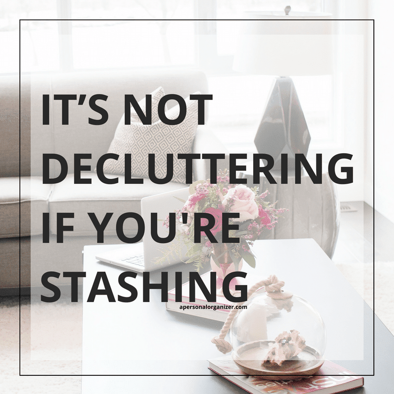 A minimalist living room with a sofa, decorative pillows, and a coffee table adorned with a flower vase and a glass cloche. Overlaid text reads, "IT'S NOT DECLUTTERING IF YOU'RE STASHING." Decluttering starts with letting go of what you don't need.