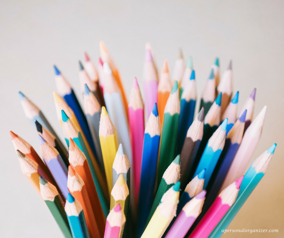 A close-up of a colorful assortment of neatly arranged, sharpened colored pencils standing upright in a container, featuring various hues including reds, blues, greens, yellows, and more. Perfect for back to school season with their pointed tips facing upward.