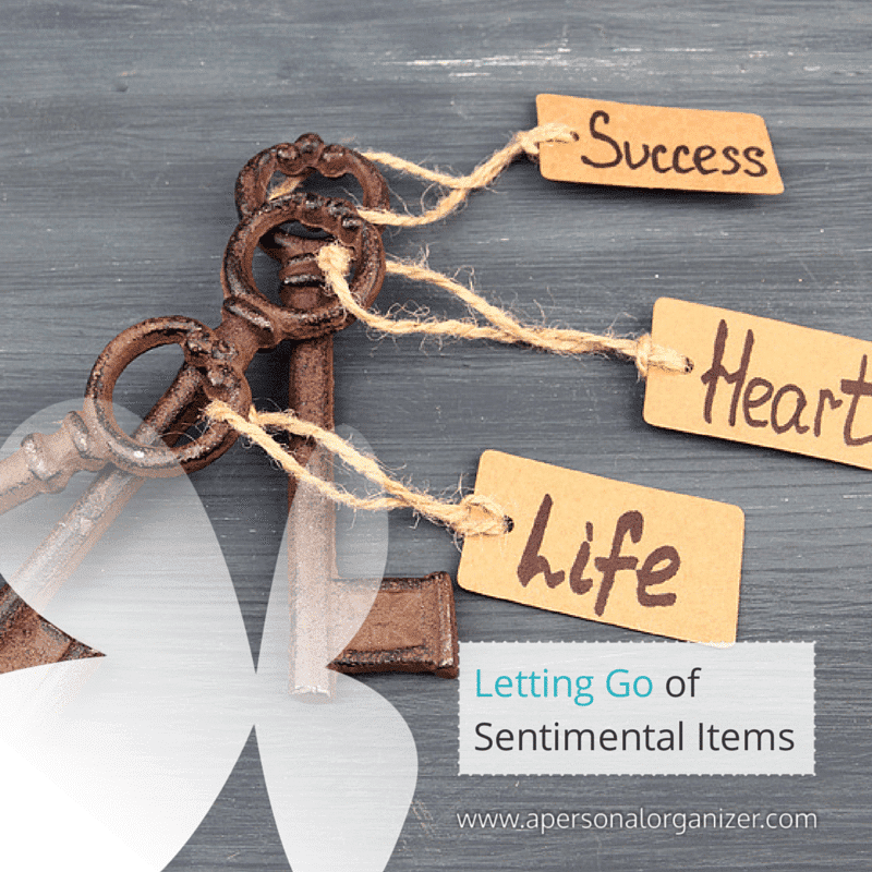 A set of three old-fashioned keys with attached tags labeled "Success," "Heart," and "Life" lie on a gray surface. A white butterfly silhouette graces the background. Text on the image reads "Letting Go of Sentimental Items" with a website link below, encouraging you to let go of sentimental items gracefully.