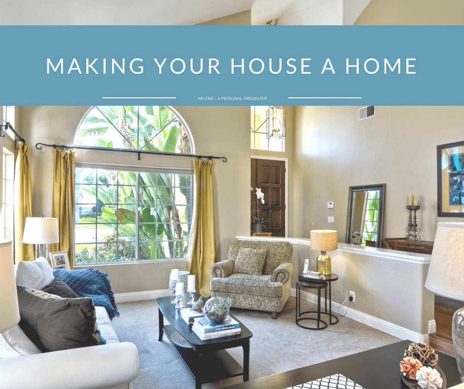 A well-lit, cozy living room with large windows, cream-colored walls, and modern decor. A beige sofa and armchair provide seating, complemented by a black coffee table and side tables. Text at the top reads "MAKE YOUR HOUSE A HOME" with a subtitle "HELENA - A PERSONAL ORGANIZER.