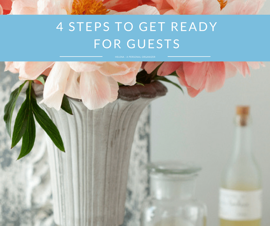A vase of pink flowers with green leaves sits on a table, accompanied by a glass bottle and a lidded glass container. A blue banner with white text across the flower arrangement reads, "4 Steps to Get Ready for Guests.