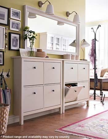 A bright room with yellow walls features two white storage cabinets with black handles, perfect for organizing a narrow entry. One drawer is open, revealing interior storage space. Above the cabinets is a large mirror and two wall sconces. Decor items and picture frames adorn the wall. A coat rack stands nearby in this inviting entrance.