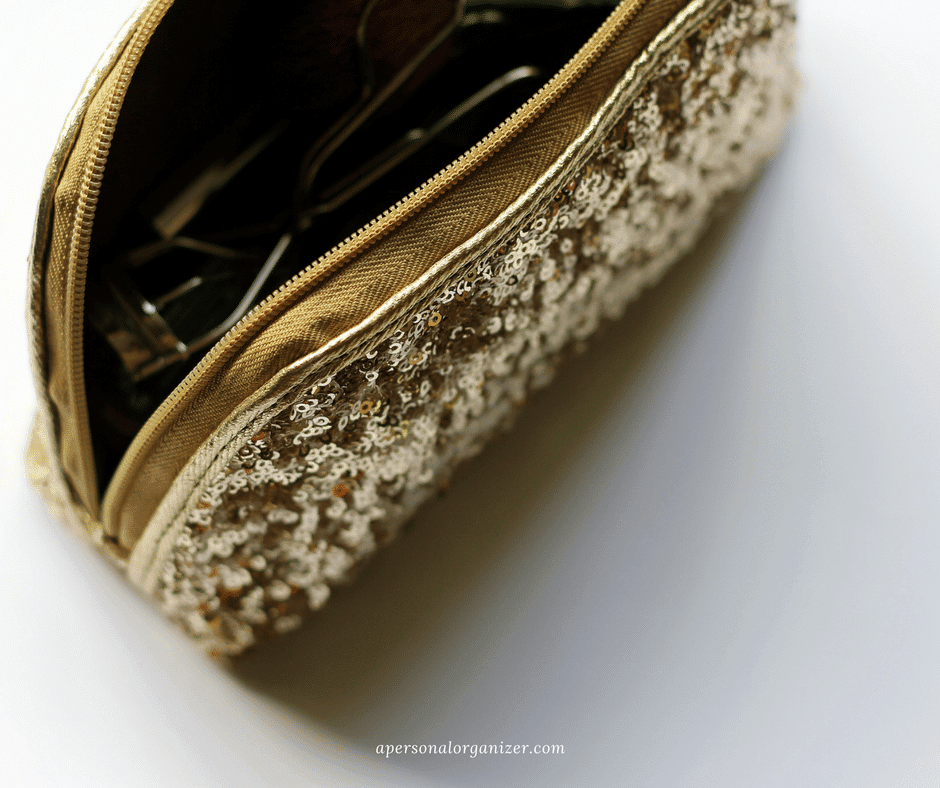 A close-up of a gold, sequin-covered makeup bag with its zipper partially open, revealing a pair of sunglasses inside. The bag's ornate texture and glimmering sequins are prominently displayed, making it perfect for your decluttering needs. The words "apersonalorganizer.com" are written at the bottom.