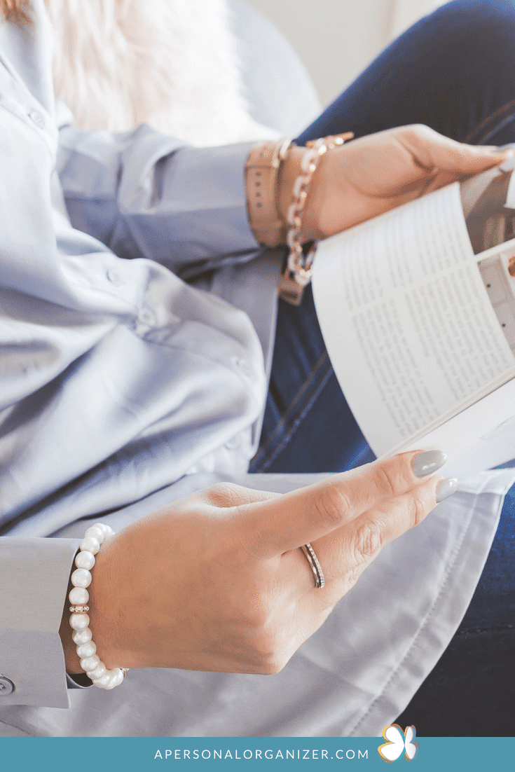 A person wearing a light blue shirt sits while holding and reading a book or magazine about how to grow your business. They are accessorized with a pearl bracelet, rings, and a watch. The image has a website URL at the bottom: "APERSONALORGANIZER.COM.