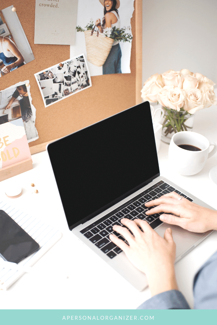 A person typing on a laptop at a bright, decorated workspace. The desk includes a cup of coffee, a notebook, and a smartphone, hinting they might be about to start a blog. A corkboard displays photos, notes, and a small vase of flowers in the background. The bottom edge of the image reads "apersonalorganizer.com".