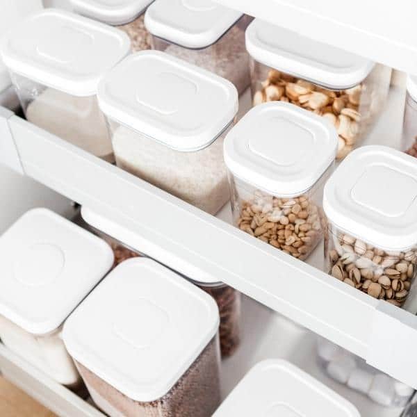 Clear containers with white lids, perfect organizing products, are neatly arranged on shelves, holding various grains and nuts. This organized storage creates a clean and minimalist look.