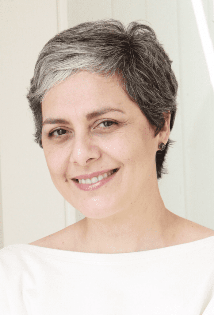 A smiling person with short gray hair and a white top stands against a light-colored background, exuding confidence as if ready to lead a curso online personal organizer.