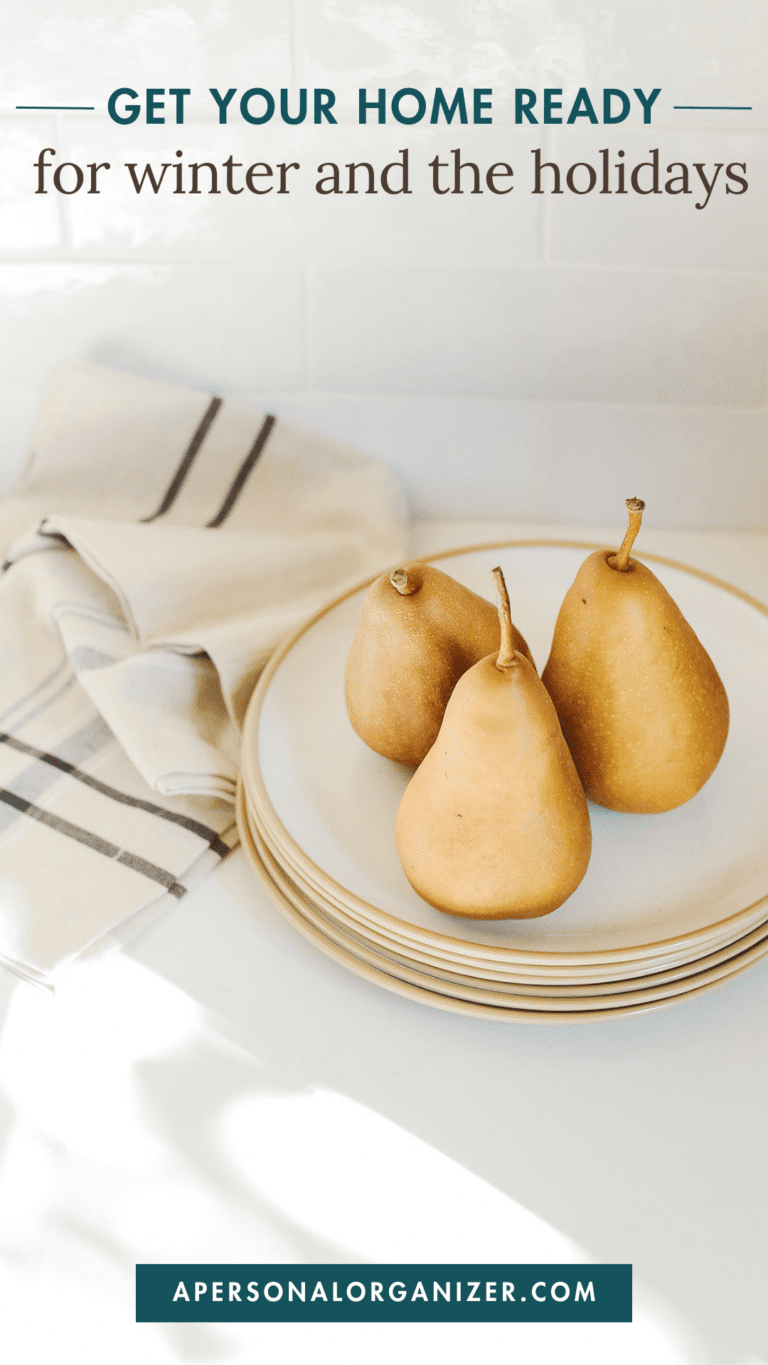 Three pears sit on a stack of white plates with a striped cloth nearby. The text at the top reads, "Organize Your Home for Winter Holidays," and at the bottom, "apersonalorganizer.com.