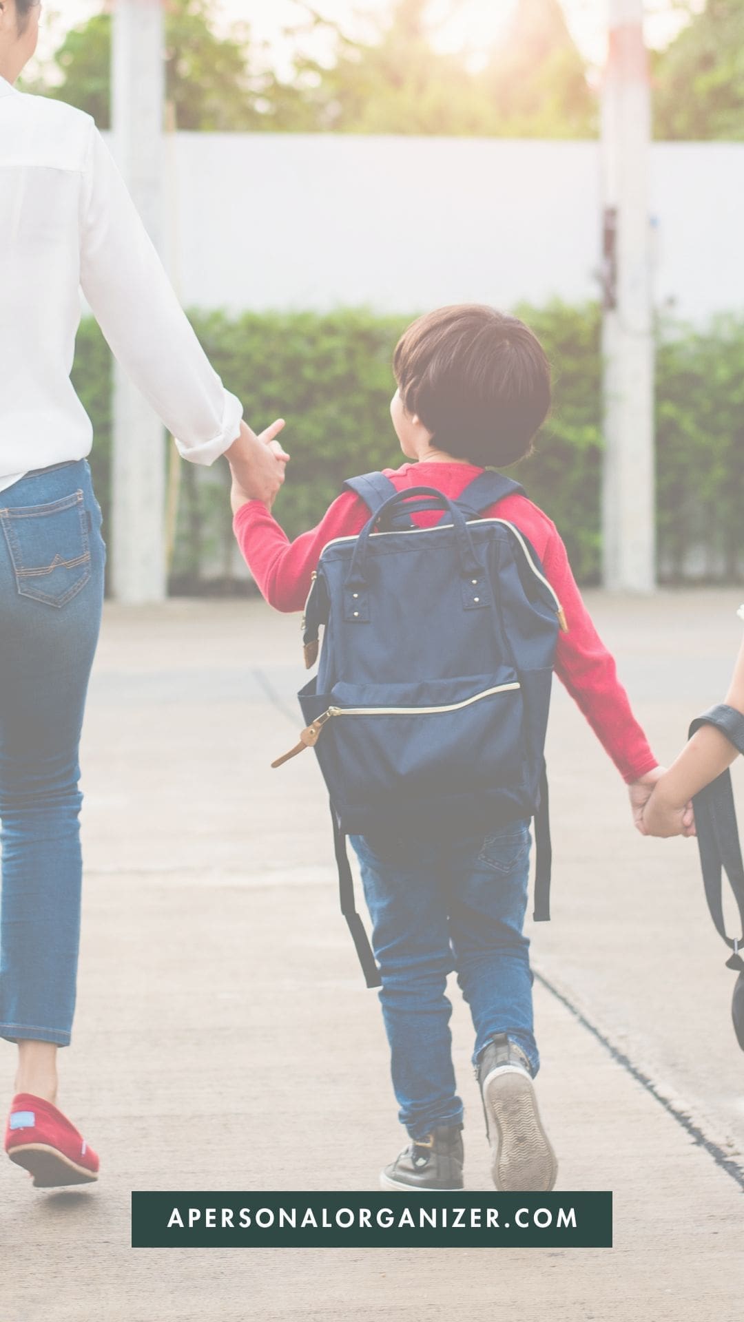 A young child with a backpack holds hands with an adult while walking outdoors, accompanied by another child. The website "apersonalorganizer.com" is displayed at the bottom, hinting at a helpful back to school shopping guide.