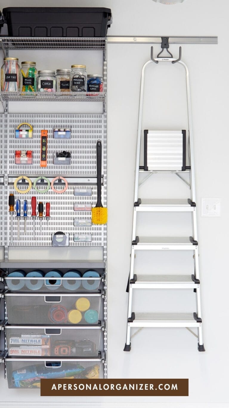 A neatly organized garage wall with shelves holding tools, paint cans, and storage bins. A silver step ladder is mounted on the wall next to the shelving. At the bottom, a label reads "APERSONALORGANIZER.COM".